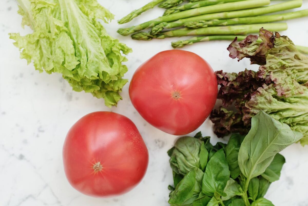 Offres Top view of fresh vegetables including lettuce, asparagus, tomatoes, and basil on marble surface.