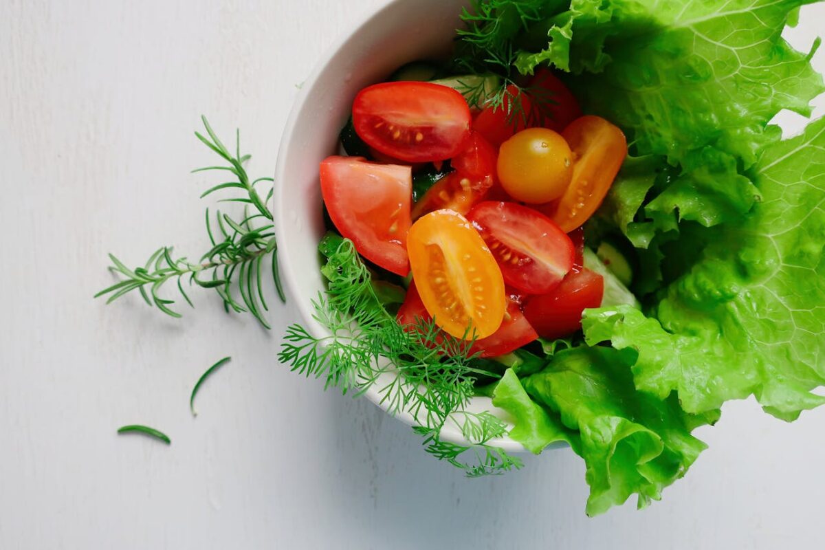 Offres Top view of a fresh vegetable salad with tomatoes, lettuce, and herbs in a bowl.