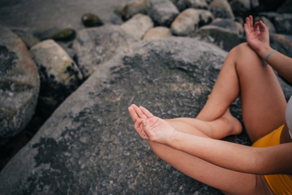 A woman in a meditative pose on a seaside rock, focusing on mindfulness and relaxation.
